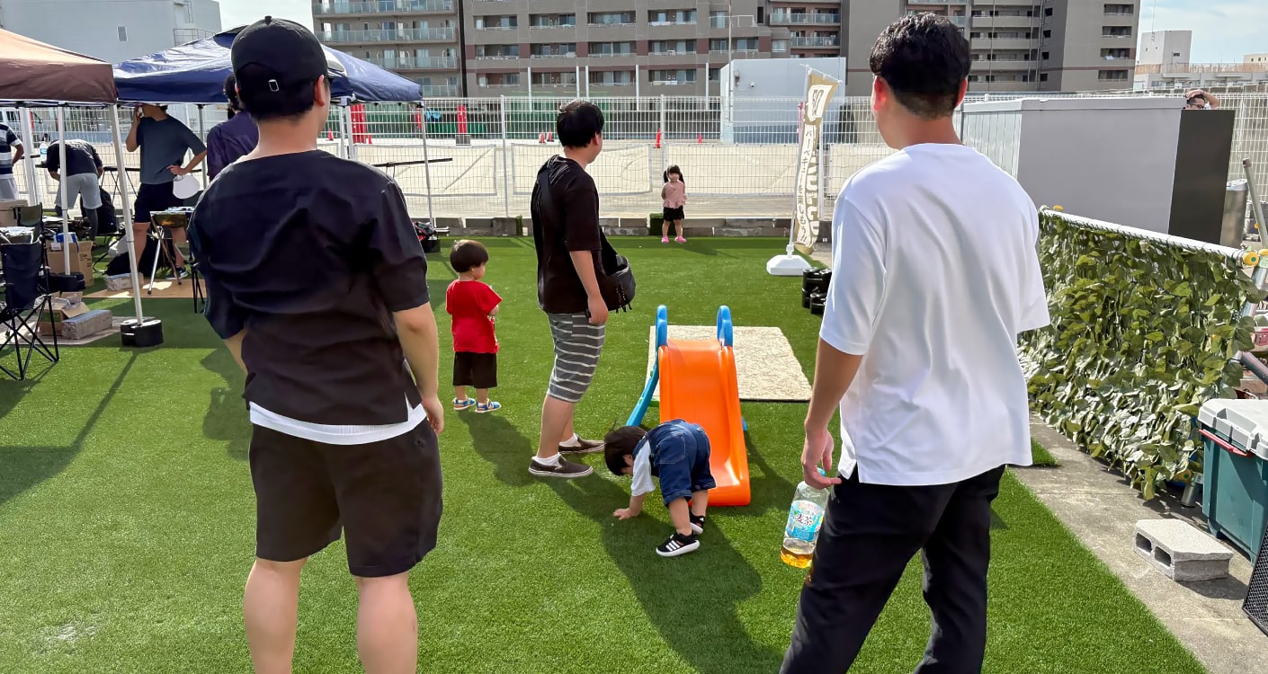 原っぱで子どもを見守る親の写真